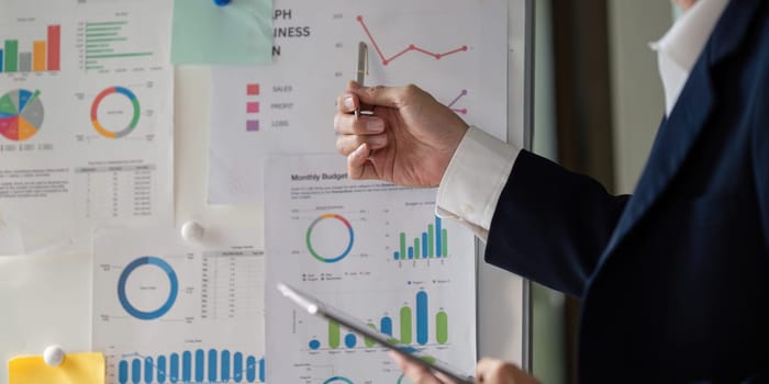 An elderly businessman holds a pen while pointing at financial charts, emphasizing the importance of data in decision-making.