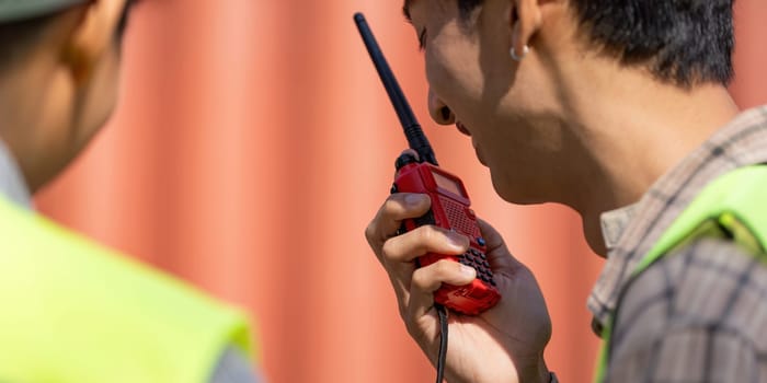 An engineer in a yellow hard hat communicates logistics via a walkie-talkie, emphasizing teamwork and safety.