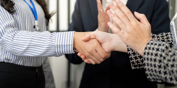 A group of business professionals applauds after a successful handshake, highlighting teamwork and mutual respect in a corporate setting.
