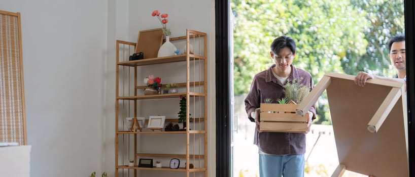 A gay couple carries boxes and plants into their new home, celebrating their move and teamwork in creating a shared space.