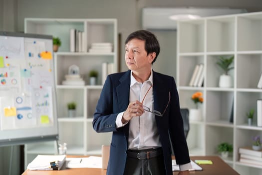 An elderly businessman stands thoughtfully in his office, contemplating his next steps in a professional setting.