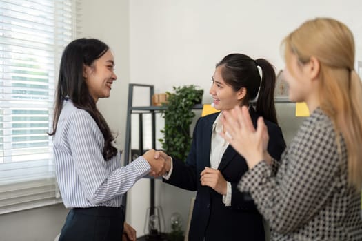 Two businesswomen shake hands while celebrating a successful partnership, highlighting teamwork and collaboration in the office.