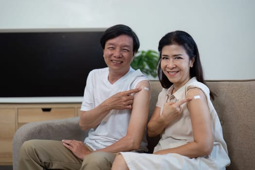 An elderly couple joyfully shows off their vaccination band-aids, celebrating health and wellness at home.