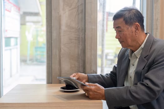 A senior businessman is absorbed in his tablet while savoring coffee, representing a blend of work and relaxation in a contemporary cafe.