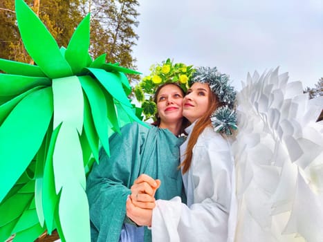 Girls wearing white and green dresses pose by the lake, embodying the enchanting meeting of winter and spring in a creative role-playing shoot.