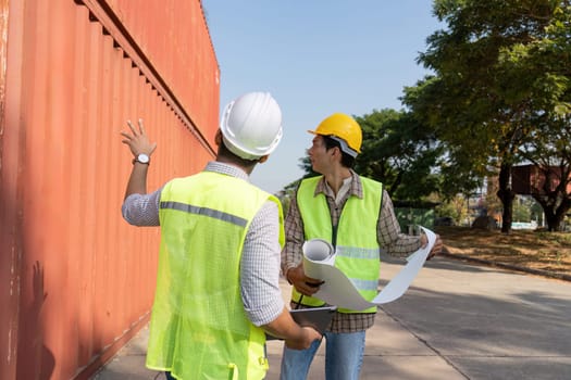 Two engineers collaborate on logistics strategies at a shipping yard, reviewing blueprints and container placements.