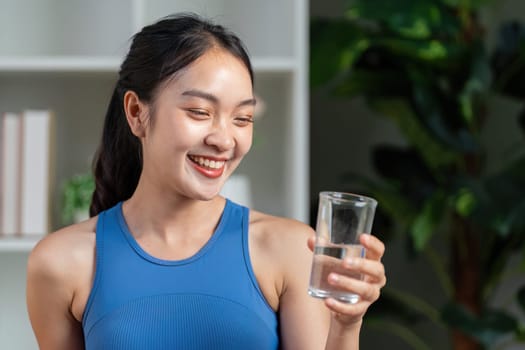 A cheerful woman smiles while holding a glass of water, emphasizing the significance of hydration and healthy living.