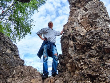 Individual poses confidently among rugged cliff formations, gazing into the distance on a pleasant day.