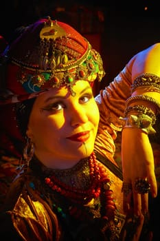 A woman in a colorful headscarf and jewelry poses in front of wall of colorful tassels