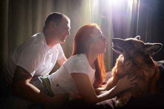 A couple enjoys playful interaction with their German Shepherd dog in a warm and inviting room.