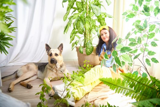 The gardener relaxes with her dog surrounded by vibrant plants in a sunny greenhouse.
