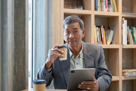 An elderly businessman sips coffee and engages with a tablet, showcasing a blend of technology and tradition in a cozy cafe.
