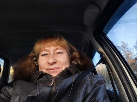 A middle-aged woman smiles while taking a selfie from the driver's seat during her adventurous road trip through scenic landscapes.