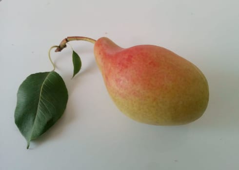 a fresh, ripe pear resting on a light surface, complemented by a vibrant green leaf. The pear exhibits a smooth texture with a blend of yellow and pink hues, making it an appealing representation of natural fruit. Ideal for food-related themes, healthy eating, or gardening.