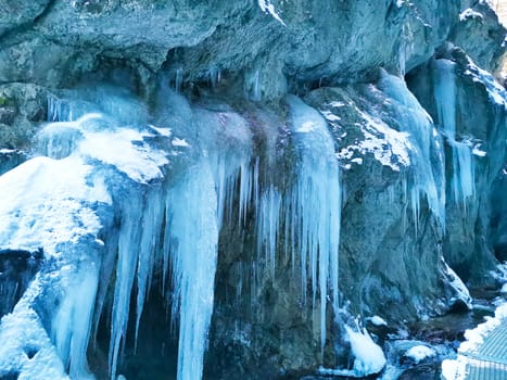 Huge icicles hang from steep cliff. Beauty in nature. Winter landscape with frozen water
