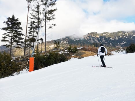 Man in ski suit and equipment stands on mountain slope. Ski run with skier. Beautiful view of the mountains, winter landscape with snow