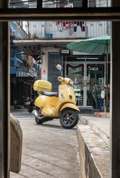 Bangkok, Thailand - Feb 09, 2025 - A Yellow vespa scooter parked on the street at a neighborhood in Bangkok city. use it as your Space for text, Design, Wallpaper and Poster, Selective focus.