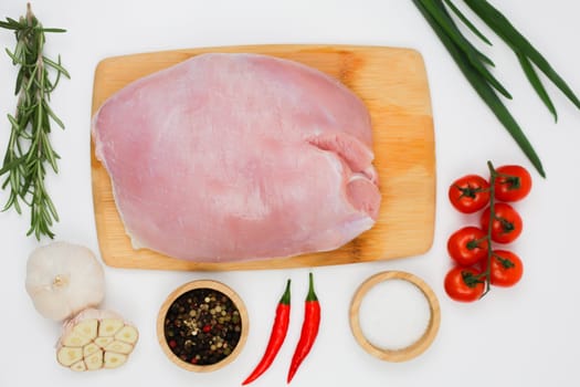 Top view in the center of a piece of turkey fillet brisket lying on a wooden cutting board on a white background surrounded by seasonings, herbs and vegetables. The concept of healthy eating, dietary and natural products, cooking. High quality photo
