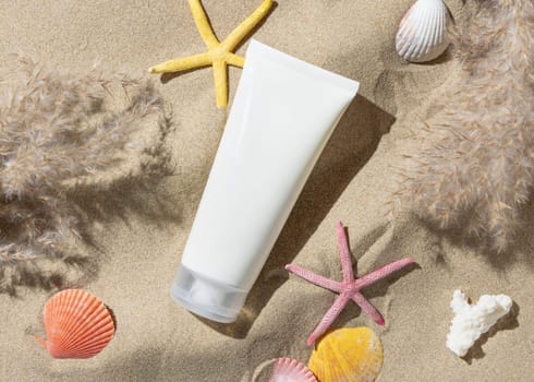 White blank cream tube, starfishes and seashells on a sandy beach top view, hard shadow. Sunscreen cosmetics mockup. Summer vacation with spf uv-protected sunbathing