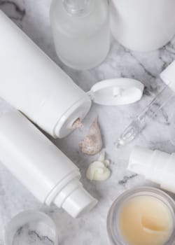 White opened cream tubes, bottles and jars on white marble table top view, mockup. Beige scrub and cream squeezed on table. Natural products for daily face care, spa procedures