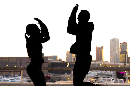 Silhouettes of a man and a woman high-fiving a skyscraper at sunset.