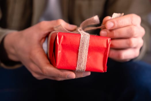 Elegant man holding gift with ribbon on the sofa at home.Celebrating Valentine's Day