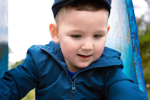 Sweet little Caucasian boy in cap having fun smiling widely sliding down the slide.