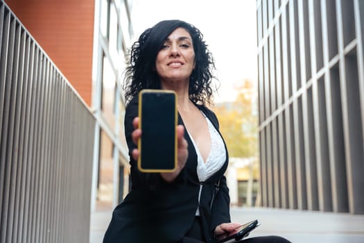 woman shows a smartphone with an empty screen for advertising or presentation, look at camera., smiling. Gadget Concept
