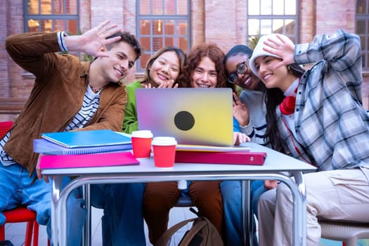 Young smiling students make a video call on a laptop. Four students wave and laugh outdoor. Concept: university life.