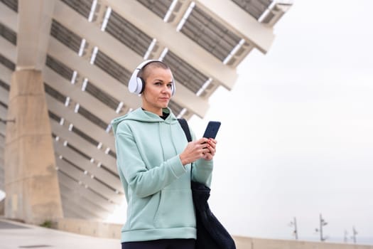 An athletic woman with headphones tired from exercising takes a break to use a cell phone messaging app.