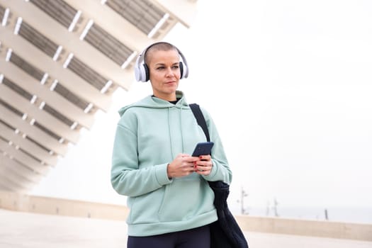 An athletic woman with headphones tired from exercising takes a break to use a cell phone messaging app.