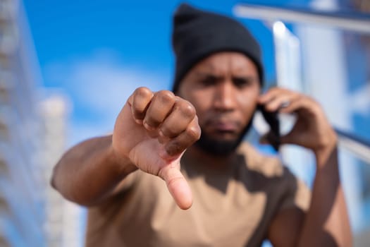 Closeup of a young pensive latin man pointing thumb down. Confident facial expression.
