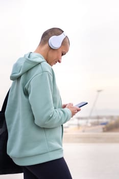 Side view an athletic woman with headphones tired from exercising takes a break to use a cell phone messaging app.