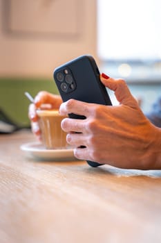 Hands of businesswoman taking a break in a cafe. A mature boss holds a phone in her hands, writes messages using an app.