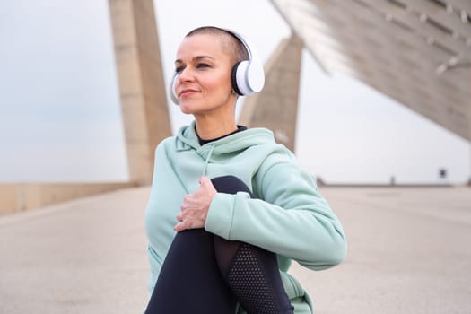 Sporty woman with sports headphones listening to music, doing concentrated sitting stretching
