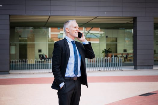 Satisfied with the results, the businessman walks down the street in front of the office building, a mature boss is talking on the telephone, writing messages.