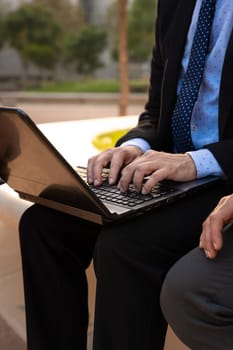 Business on the move: Businessman working on his laptop on the street. Man Hands Type On His Laptop Outdoors