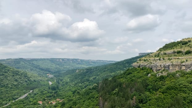 Scenic view of the Garga Bair Hill in Veliko Tarnovo, Bulgaria. Lush green valley with a winding road below. A cloudy sky overhead - Europe