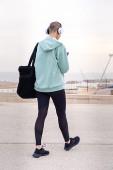 An athletic woman with headphones tired from exercising takes a break to use a cell phone messaging app.