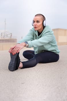 Sporty woman with sports headphones doing stretching sitting concentrated outdoors.
