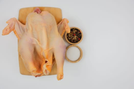 Raw processed chicken carcass lying on a white background on a wooden board with spices and salt in wooden bowls with space for text. The concept of cooking, wholesome and healthy food, recipes. High quality photo