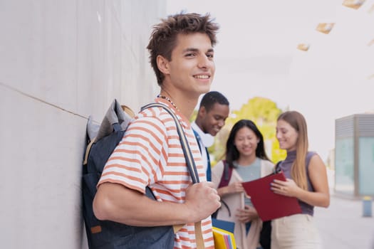 Multiracial group of teenage students talking together about exam and homework. Happy teenager smiling taking a break standing on university campus holding backpack.