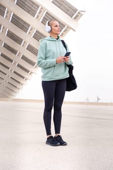 An athletic woman with headphones tired from exercising takes a break to use a cell phone messaging app.