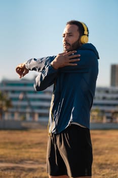 Young latin sportsman with sports headphones doing stretches with water bottle on the floor.