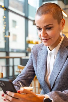Satisfied with the results, the businesswoman who takes a break in a cafe looks at the results with satisfaction. A mature boss holds a phone in her hands, writes messages and reads news online, using an app.