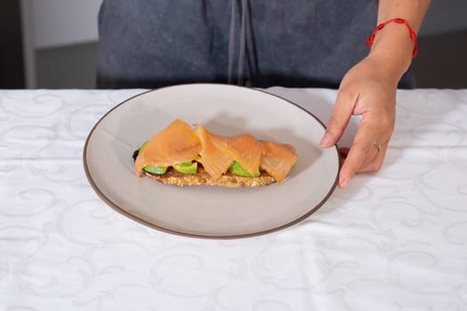 Close-up of a young woman's hands holding a plate with salmon and avocado toast.concept: healthy eating