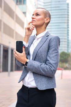 Satisfied with the results, the businesswoman walking on the street outside the office building, a mature boss holds a phone in her hands, writes messages and reads news online, using an app.