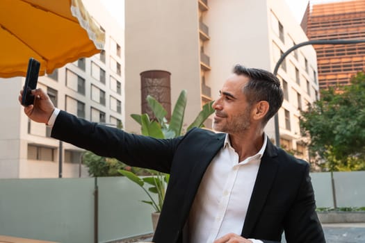 Middle aged man sitting happily taking a selfie with cell phone.
