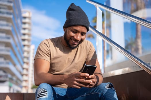 Happy Latin man smiling while browsing the internet with a telephone feeling of happiness outdoors.