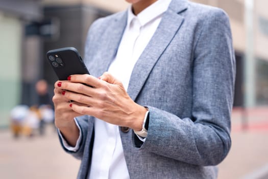 Satisfied with the results, the businesswoman walking on the street outside the office building, a mature boss holds a phone in her hands, writes messages and reads news online, using an app.